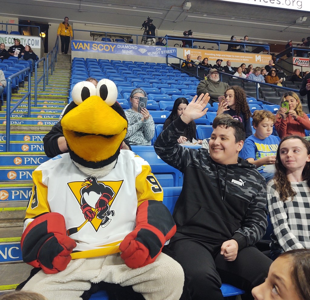 Tux the Penguin the Wilkes-Barre/Scranton Penguins Hockey team mascot sits next to one of our 6th grade students inside the hockey arena.