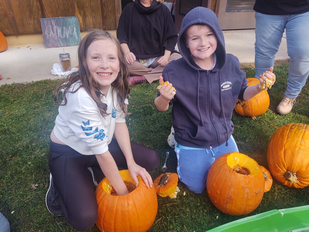 a little girl has her hand inside a pumpkin scooping out its insides and a little boy has pumpkins guts oozing out his fingers.