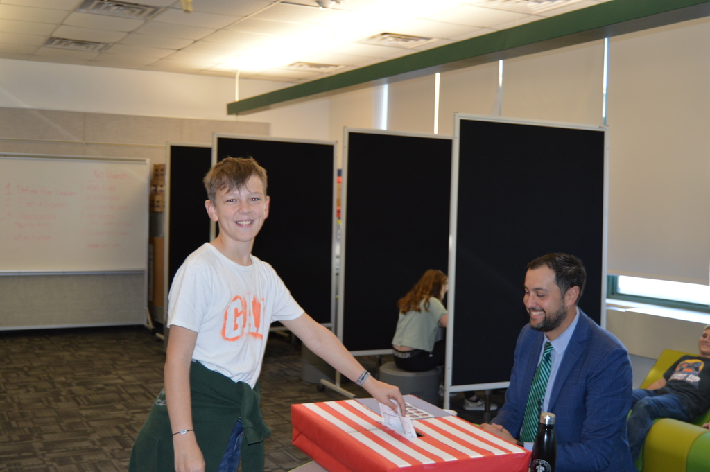 A student places his ballot in the ballot box for student council elections. Seated at the table in front of the ballot box is building principal, Mr. Carpentieri.