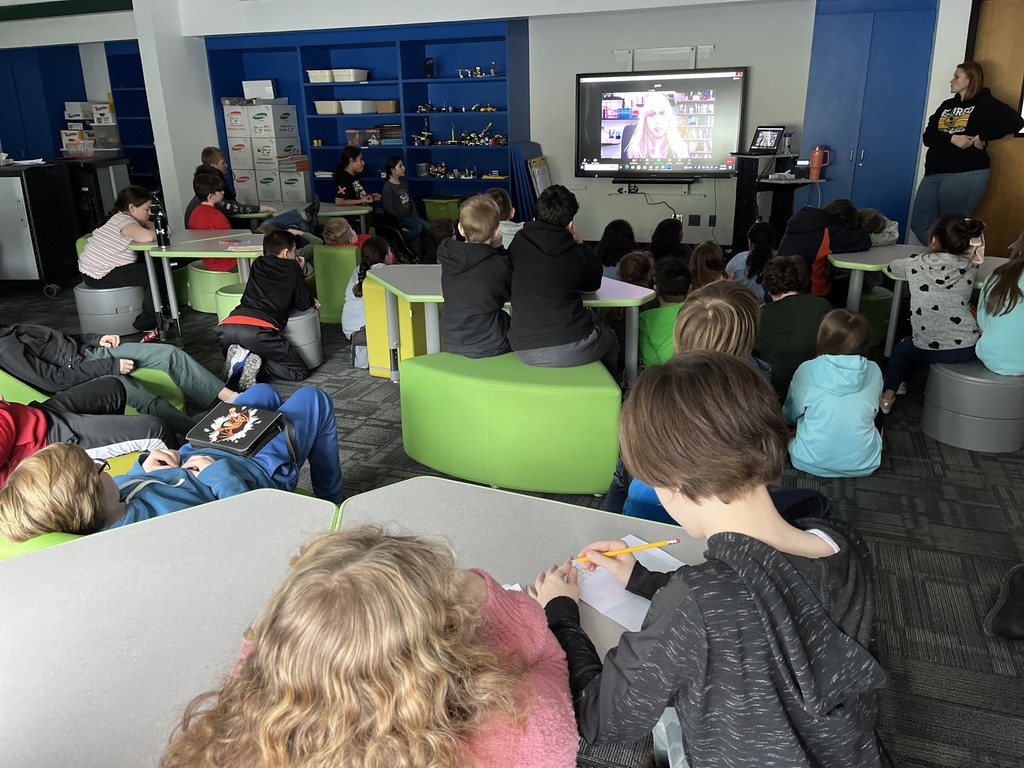 Image of students sitting down listening to bestselling author, Ellen Potter, whose image is projected on the Smartboard during a virtual lesson.