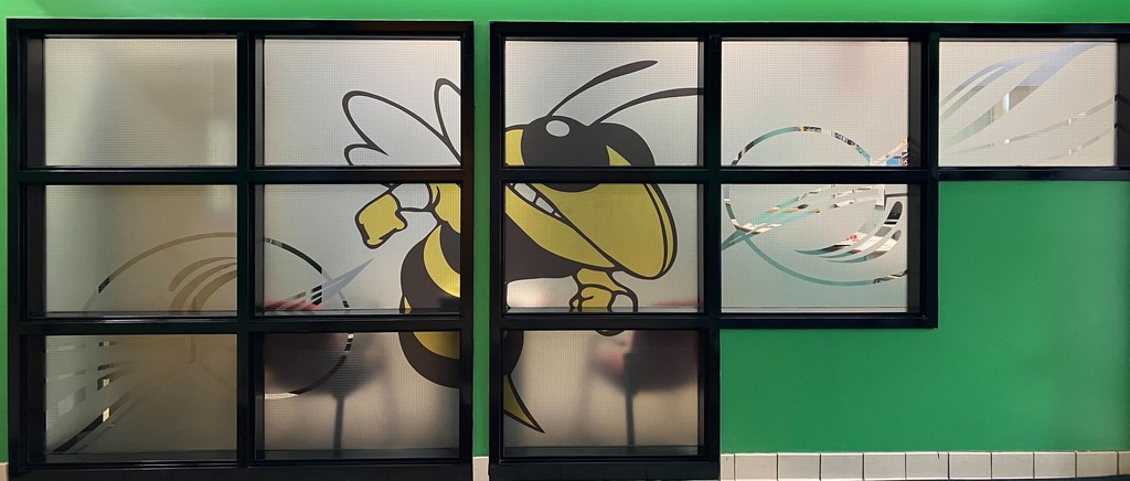 Image of a set of windows with a yellow jacket decal against a green wall.