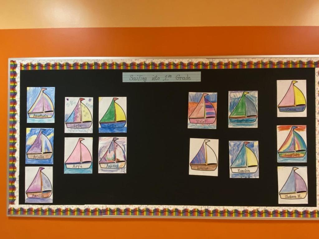An orange wall with a black bulletin board with individual pictures  of sailboats that have been colored by students