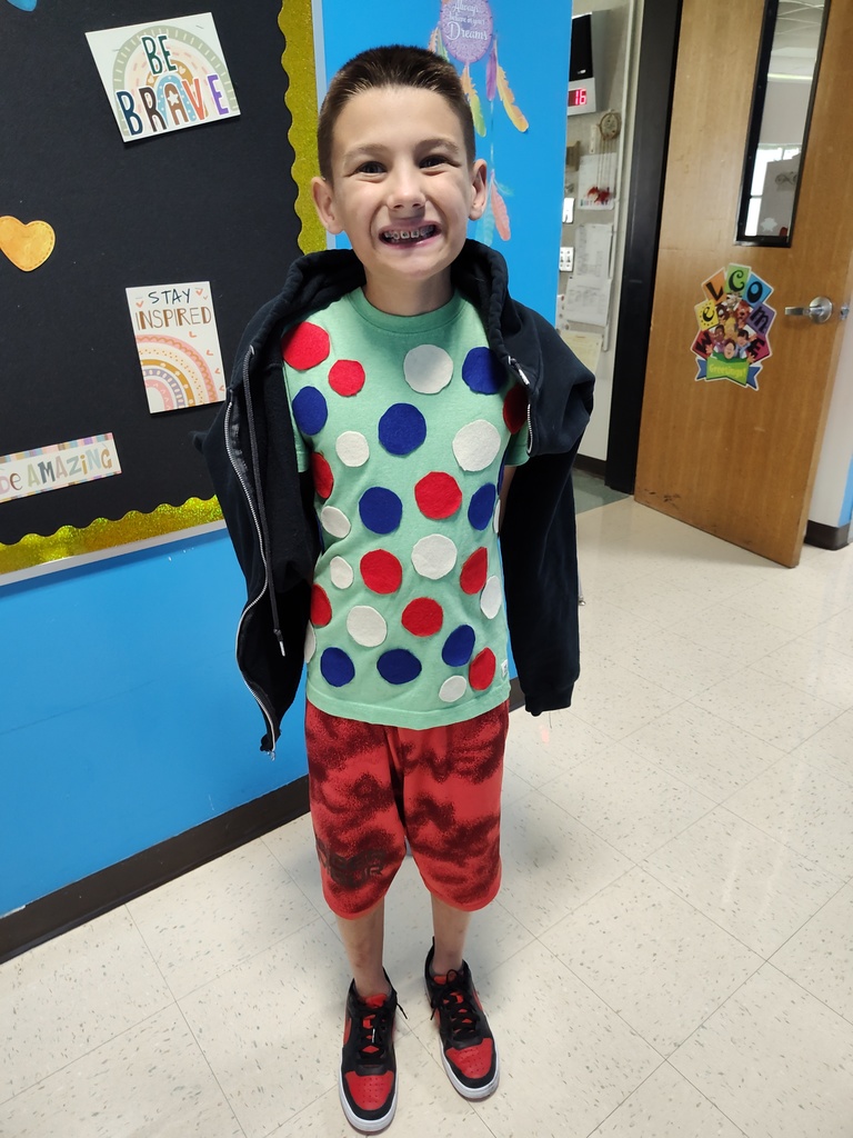 A student wearing a green shirt with blue, white and red polka dots smiles as the camera