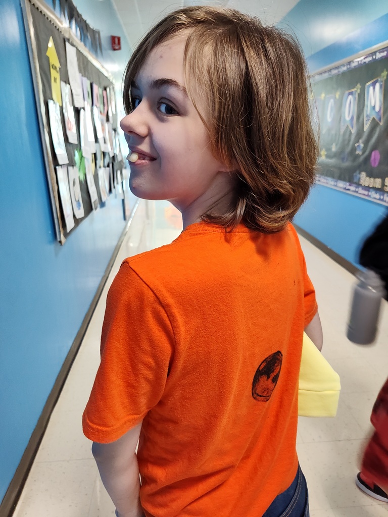 A student in an orange shirt with a black dot smiles at the camera