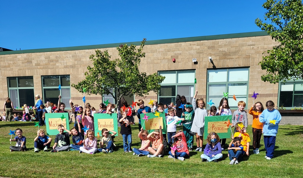 Students pose in front of signs that read Mackenzie Pinwheels for Peace