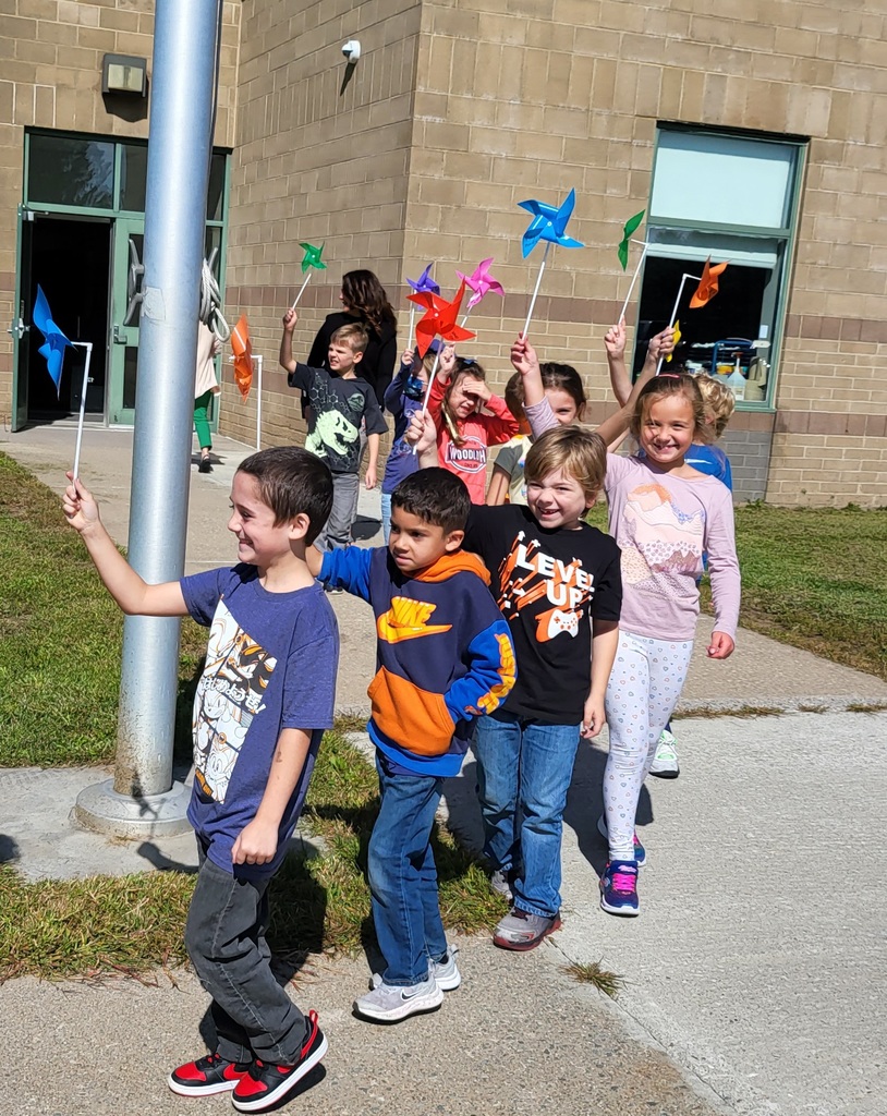 Image of students parading in front of a school building waving colorful pinwheels